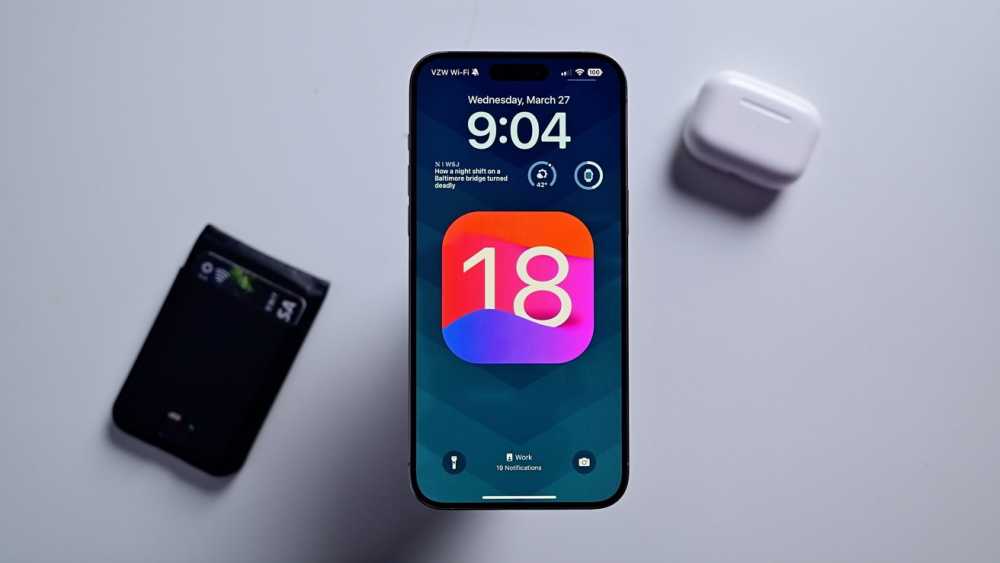 一部显示iOS 18图标的iPhone锁屏。附近有一个钱包和AirPods盒子。