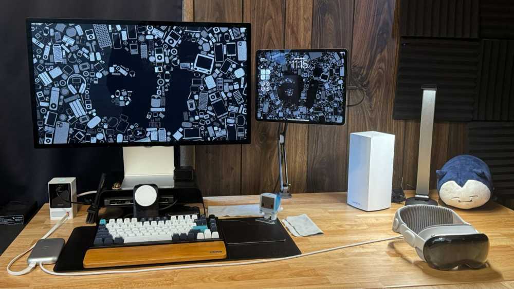 An iPad Pro connected to a Studio Display with a keyboard and trackpad below. Apple Vision Pro is on the desk.