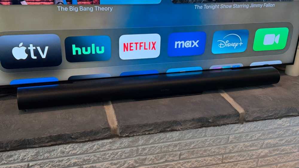 电视屏幕上显示着Apple TV、Hulu、Netflix和Disney+等流媒体应用，以及一款黑色Sonos音响放在石材表面上.