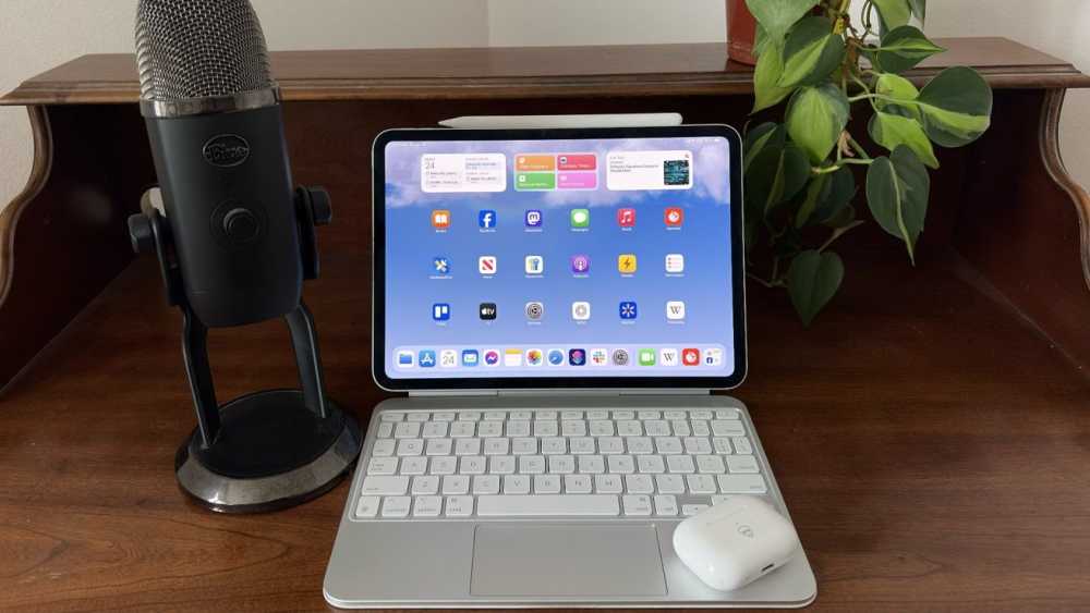 iPad Pro with keyboard on wooden desk, large microphone on left, and leafy plant on right.