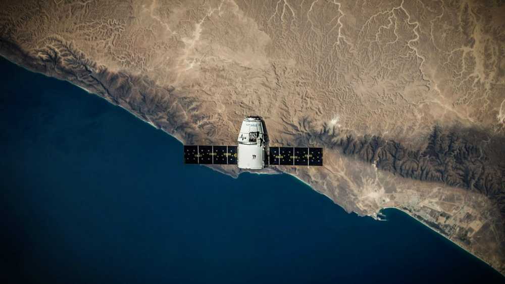 一颗卫星在蓝色海洋上空和崎岖的沙滩沿岸轨道上方,显示复杂的自然地形模式。