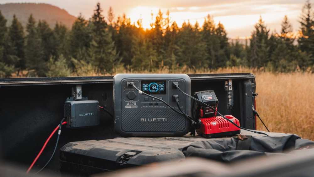 Portable power station and charger in truck bed against sunset with trees in the background.
