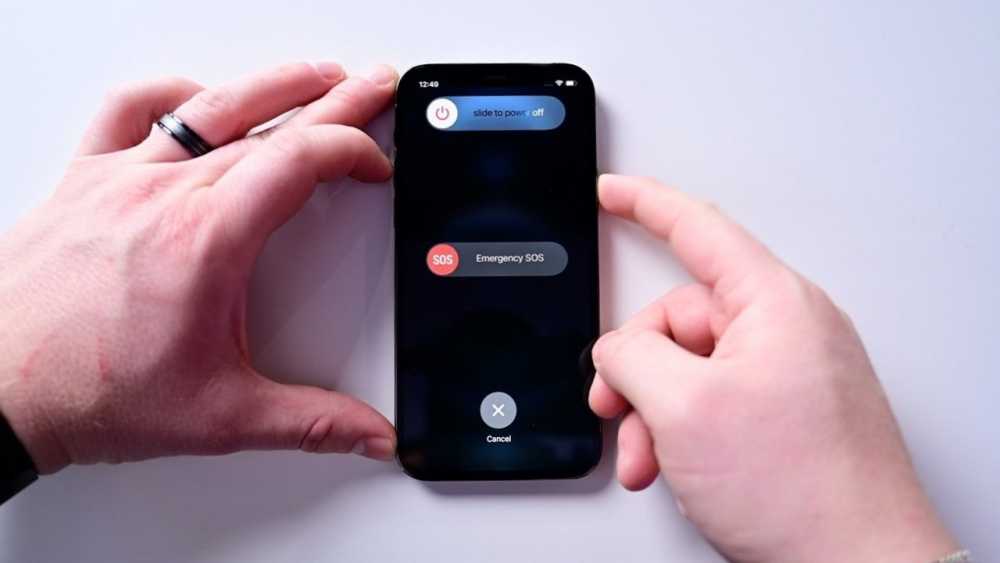 Hands holding a smartphone displaying emergency SOS and power off options on a white surface.