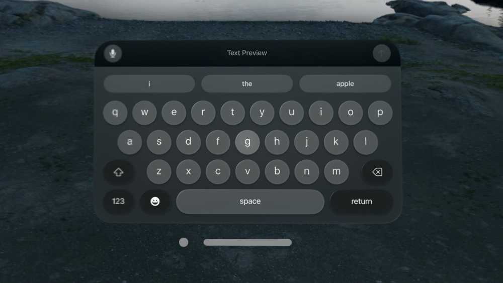 Virtual keyboard with rounded keys displayed over a rocky landscape, featuring suggested words 'i,' 'the,' and 'apple' above the keyboard layout.