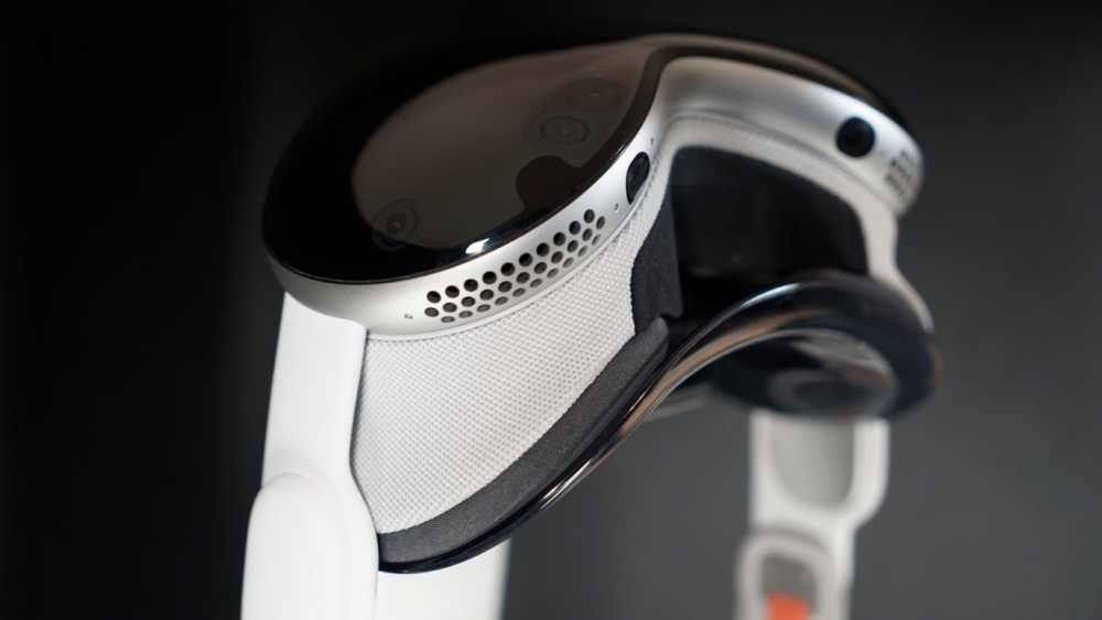 Futuristic VR 头显 with a sleek design, featuring a shiny black front, white sides, and circular ventilation holes on a silver band, seen against a dark background.