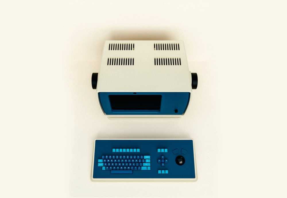 Retro computer with a blue screen and white casing, accompanied by a blue and gray keyboard with circular controls and directional arrows.