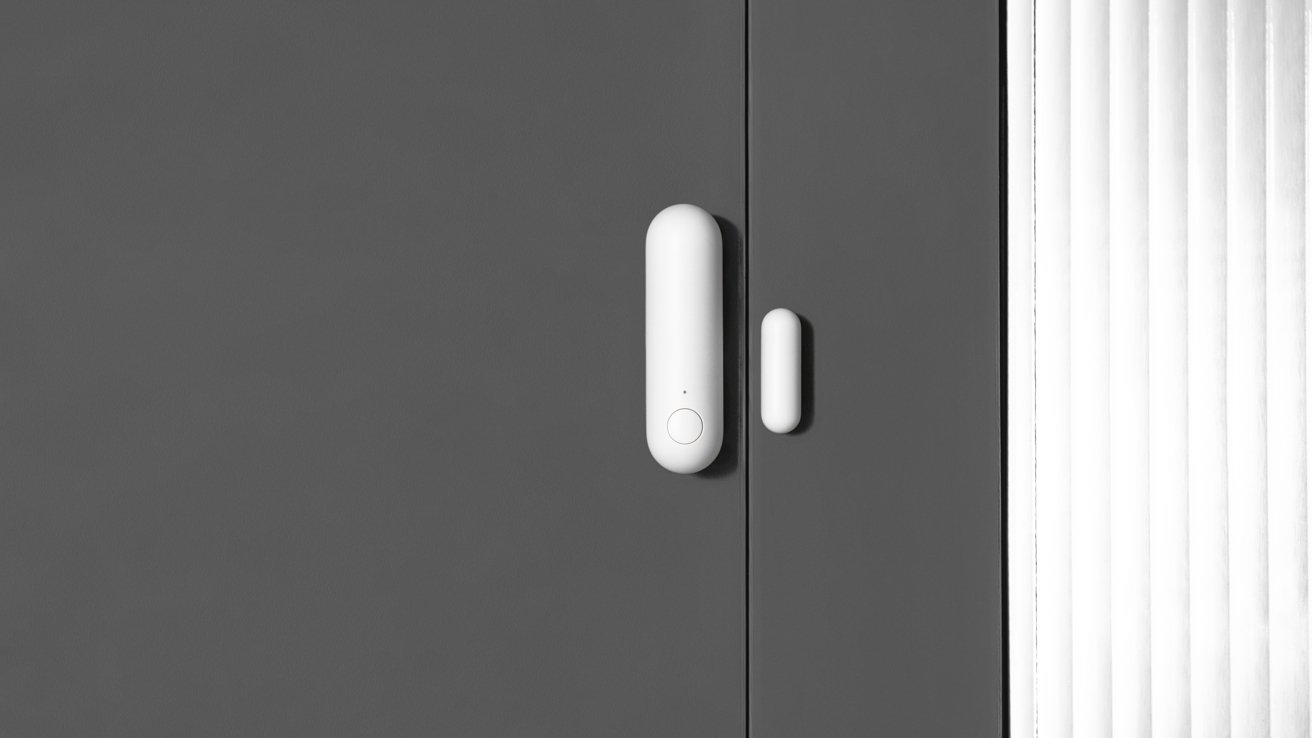 Gray door with a white cylindrical handle and sensor, adjacent to a section with narrow white vertical panels.