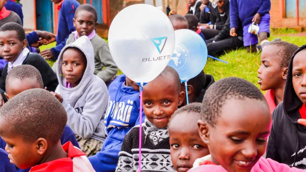 Children sitting on grass, some holding balloons, with one child in the foreground smiling.