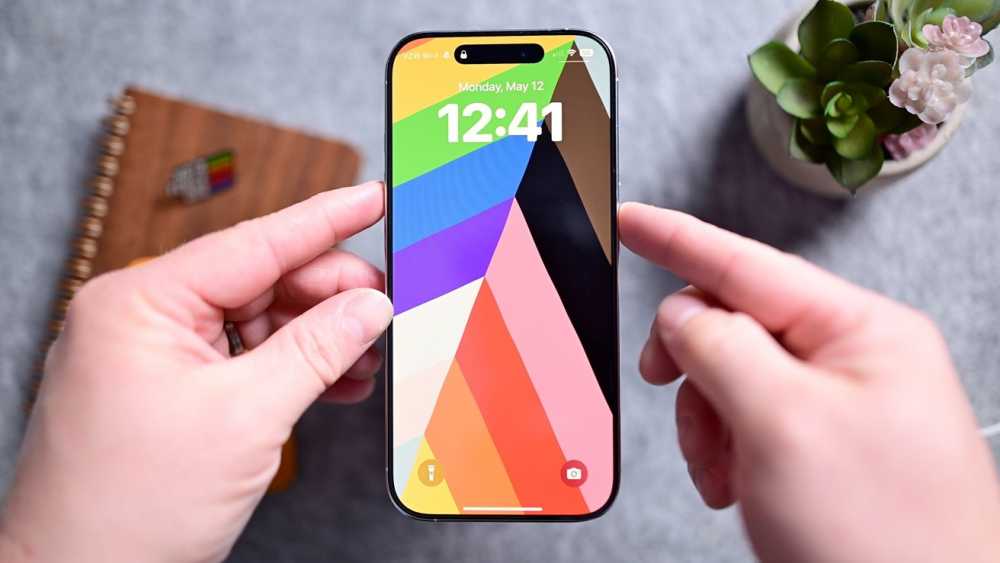 iPhone 在灰色桌面上显示彩色块壁纸，上面显示时间