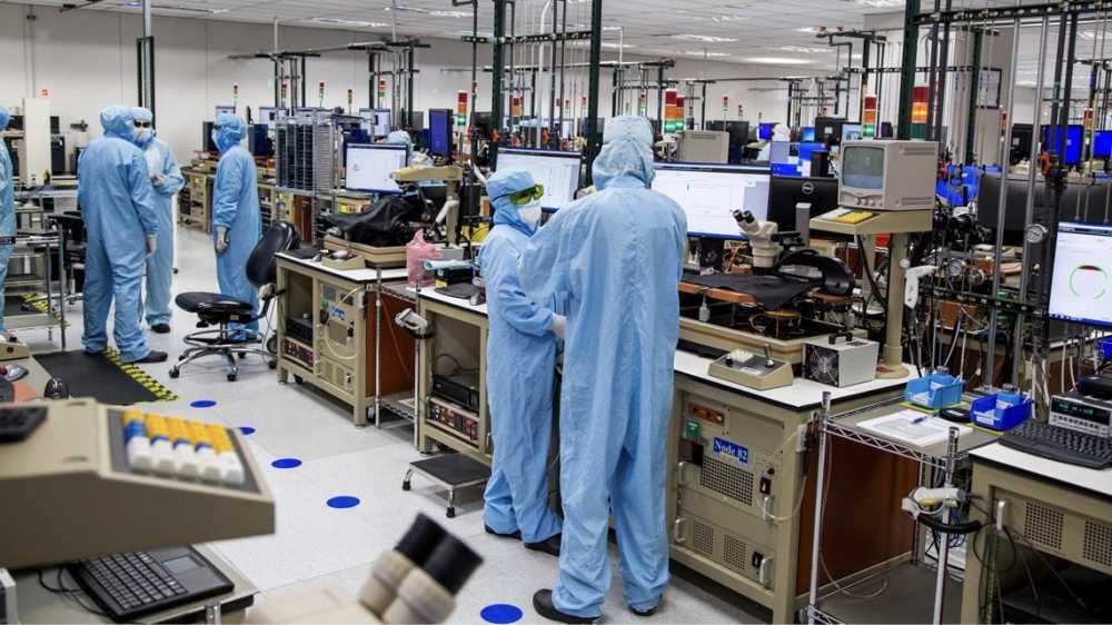 People in blue protective suits working in a high-tech laboratory with computers and scientific equipment.