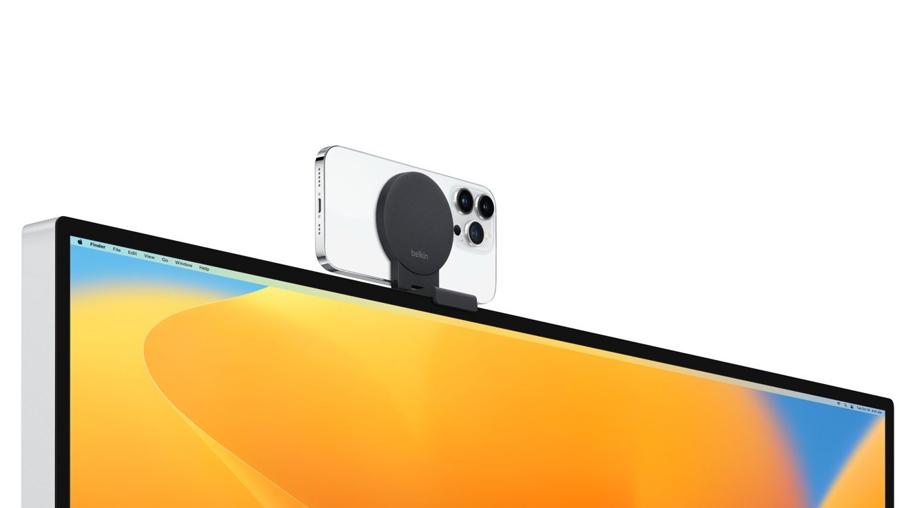 Smartphone mounted on a computer screen using a round, black accessory against a gradient orange and blue desktop background.