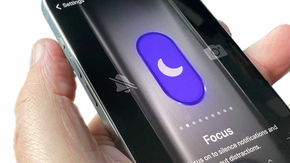 Hand holding a smartphone displaying a purple crescent moon icon for focus mode, with parts of the screen and hand visible.