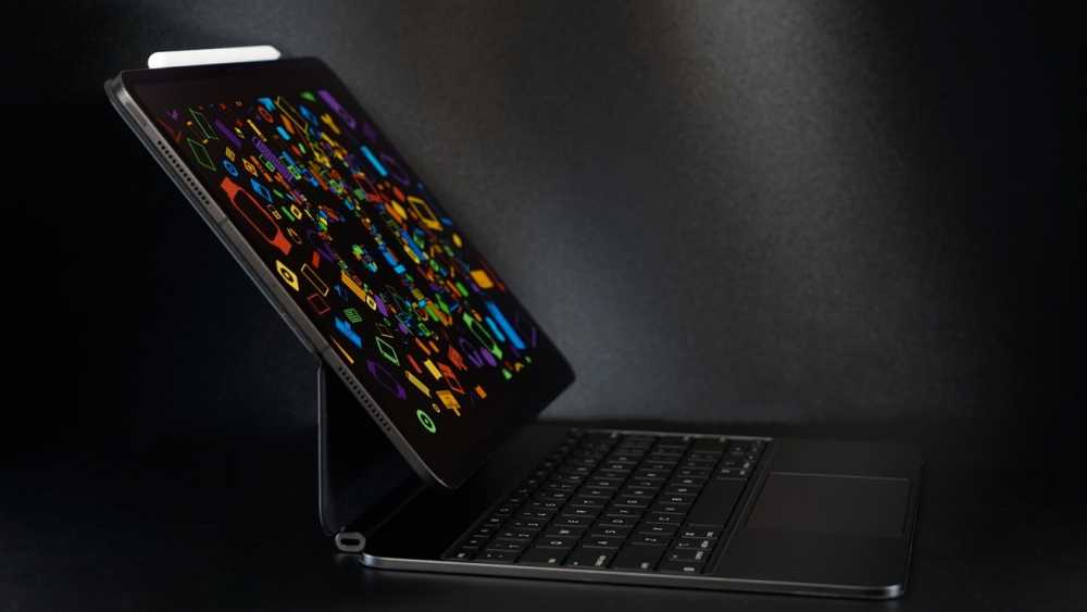Open laptop with a colorful geometric pattern on the screen against a dark background, featuring a visible keyboard and trackpad.