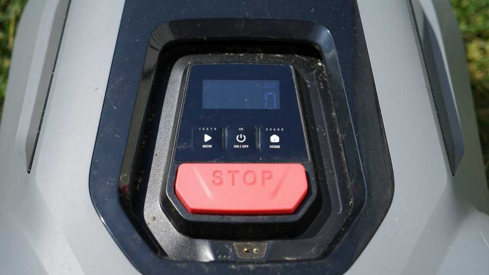 Close-up of a control panel featuring a large red stop button, small display screen, and various function buttons on a lawn mower.