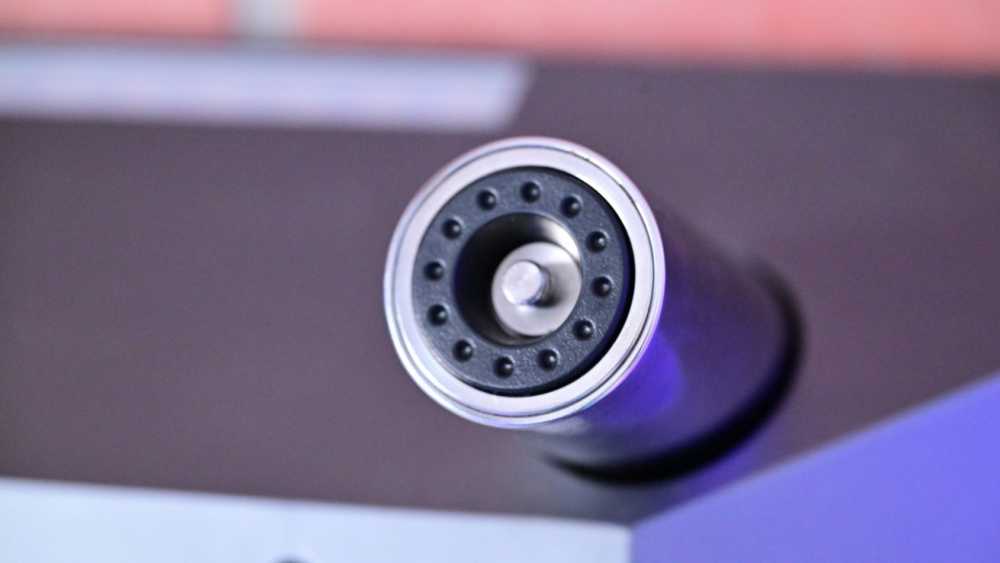 Close-up of a microphone's circular top with a metal grille and small round openings, mounted on a cylindrical body.
