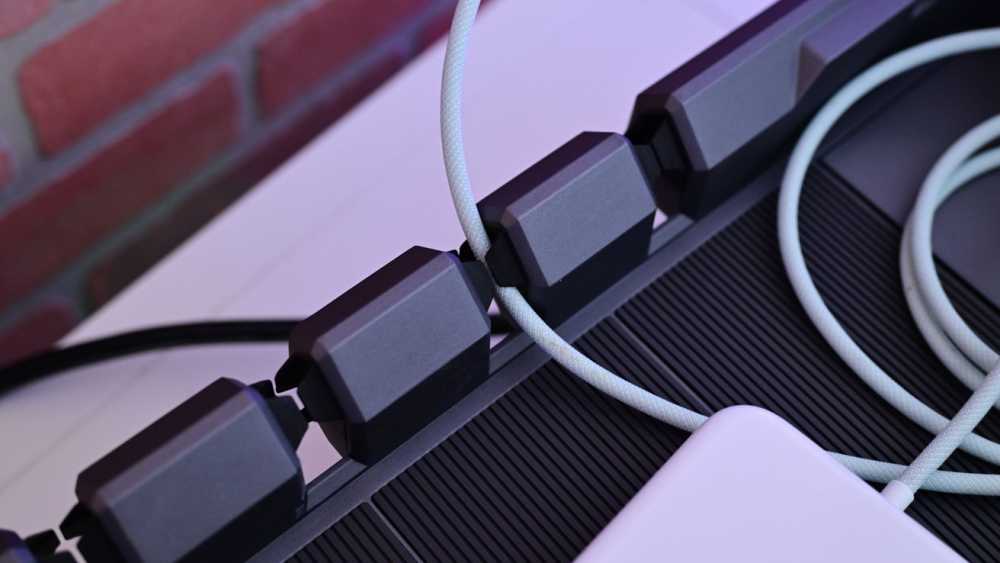 Close-up of a row of upright plastic Lego bricks against a ridged surface, with a coiled gray cable passing through gaps and a red brick background.