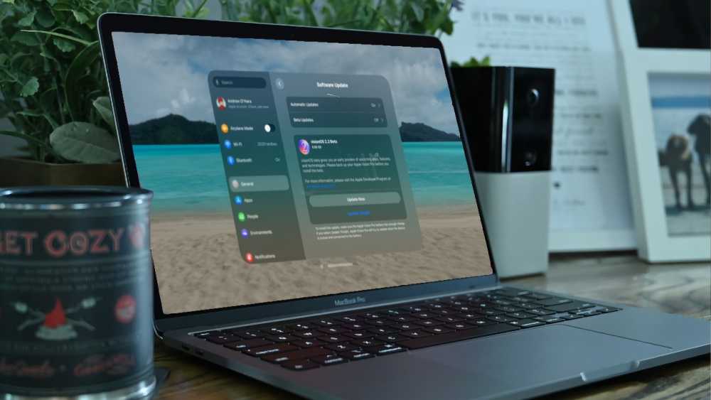 Laptop displaying software updates with a tropical beach wallpaper in the background, surrounded by potted plants, framed photos, and a candle on a wooden desk.
