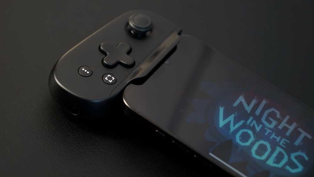 A black mobile gaming controller attached to a smartphone displaying the game title 'Night in the Woods' against a dark background.