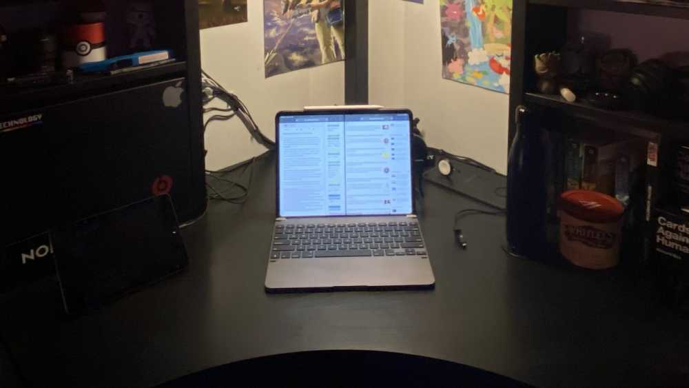 Laptop with split-screen display on a black desk surrounded by shelves with various items and colorful wall posters.