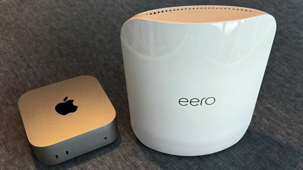 Silver device with an apple logo and a white, curved router labeled 'eero' on a gray surface.