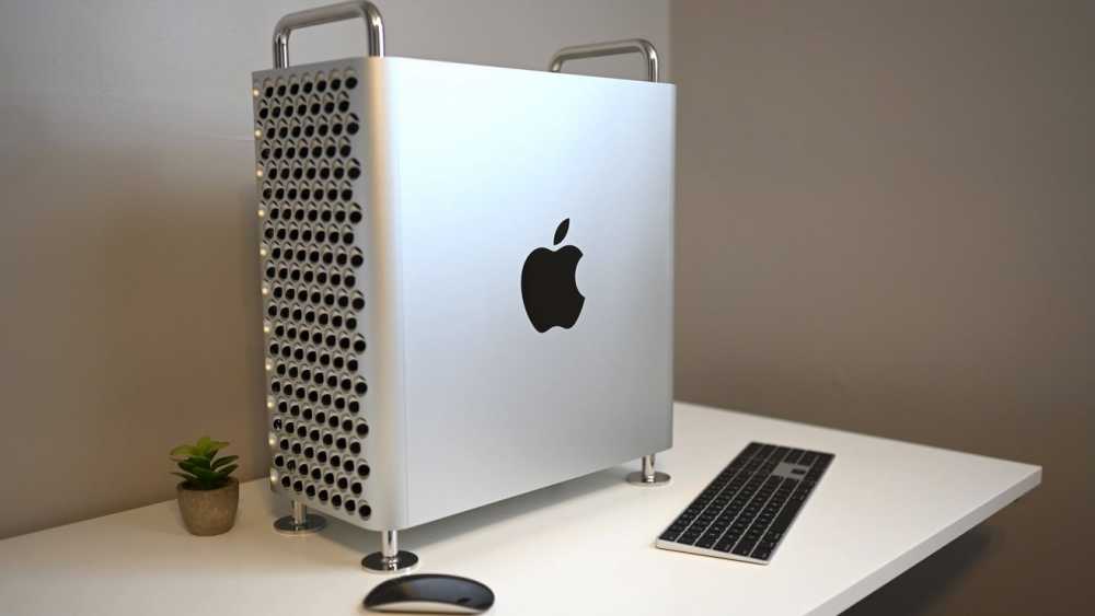 Silver computer tower with a perforated side, black apple logo, silver handles, on a white desk with a small plant, keyboard, and mouse.