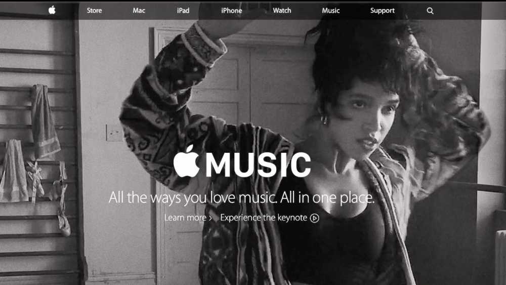 Black and white scene with a person adjusting hair, wearing a patterned jacket, and Apple Music text displayed prominently.