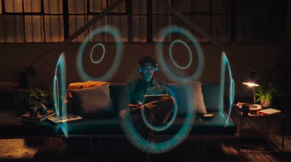 Person wearing headphones sits on a sofa with glowing circular blue patterns around them, a laptop, and a cozy, dimly lit room with plants and a lamp nearby.