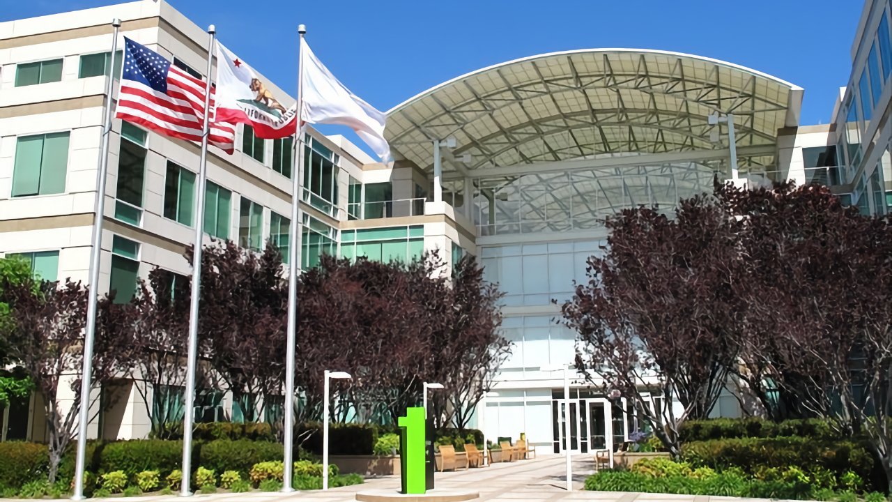 Modern office building with three flags, trees, and a large glass entrance canopy under a clear blue sky.