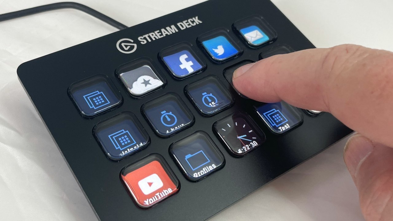 A hand pressing a customizable Stream Deck button panel featuring app icons like YouTube, Facebook, Twitter, and email on a white surface.