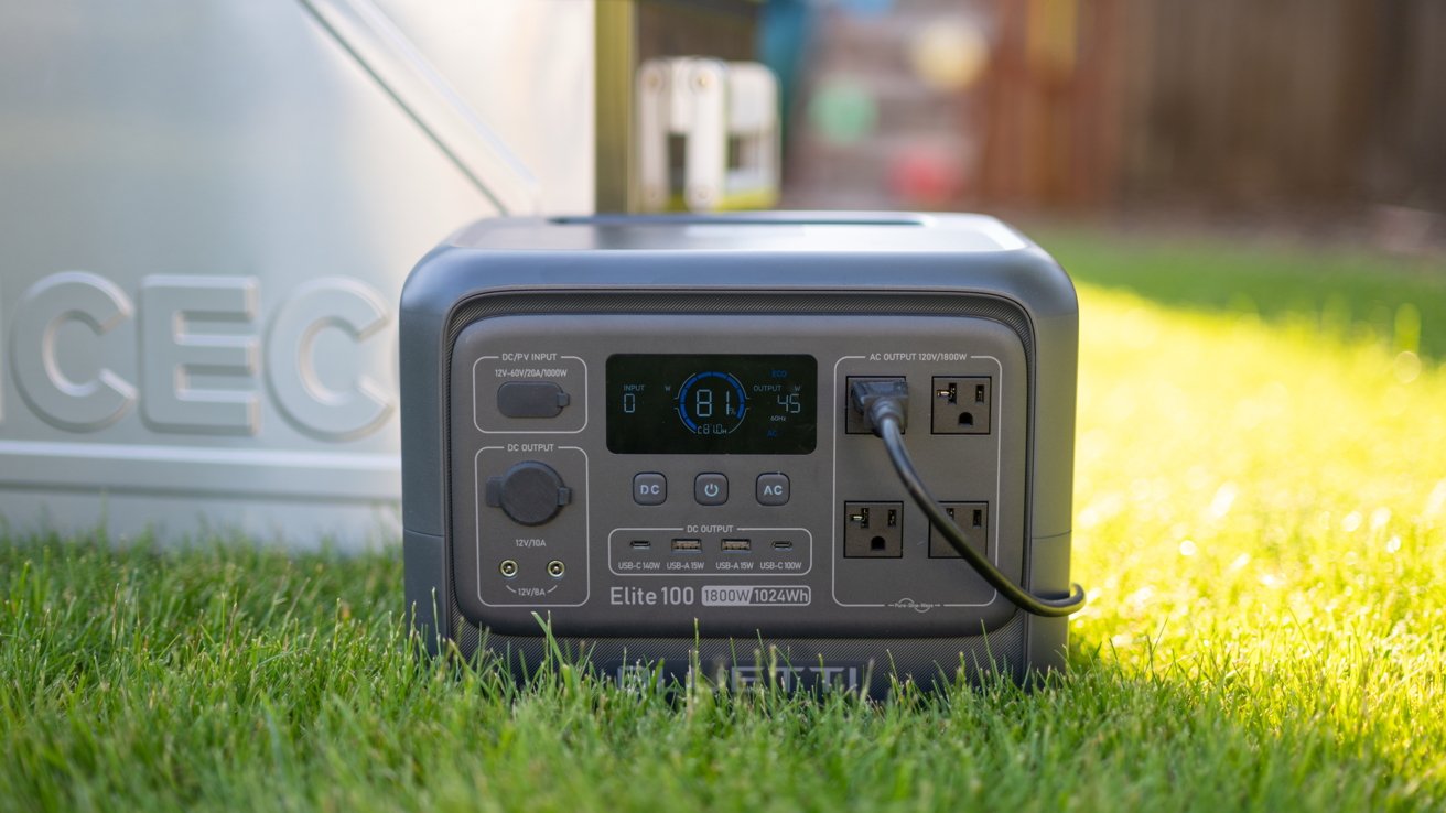 Portable power station with multiple outlets and an LED display on green grass, sunlight creating a bright ambiance.