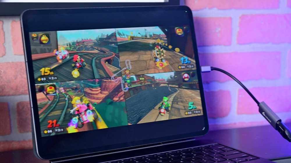 A laptop screen displays a split-screen multiplayer racing video game with four players on colorful tracks.