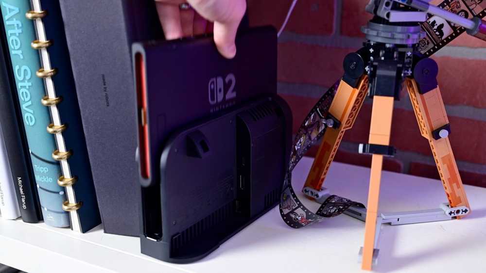 Person docking a handheld device next to books and a colorful tripod on a shelf.