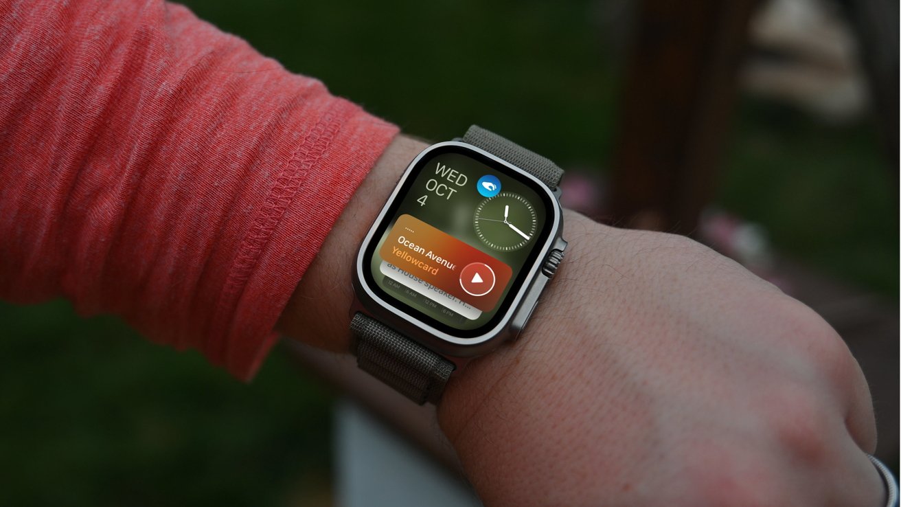 Person wearing a smartwatch displaying the date, time, and a music player with 'Ocean Avenue' by Yellowcard. Bright red sleeve visible on the wrist.