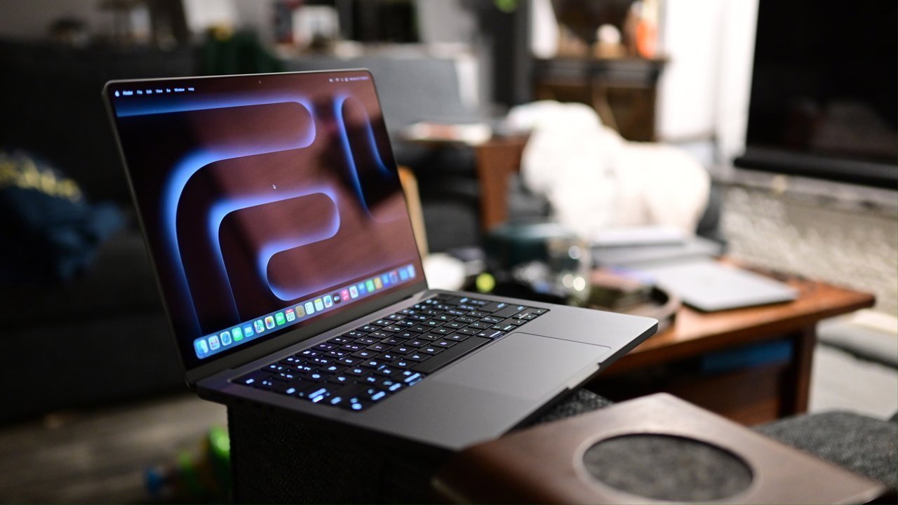 Open laptop with a glowing screen displaying abstract design, placed on an armrest in a cozy living room setting with a sofa and a wooden table in the background.