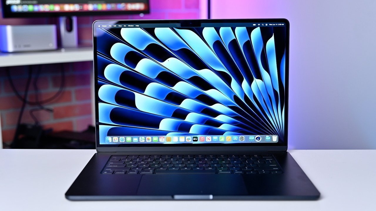 Laptop displaying a dynamic blue and black abstract pattern on screen, set on a desk with blurred background including technology equipment.