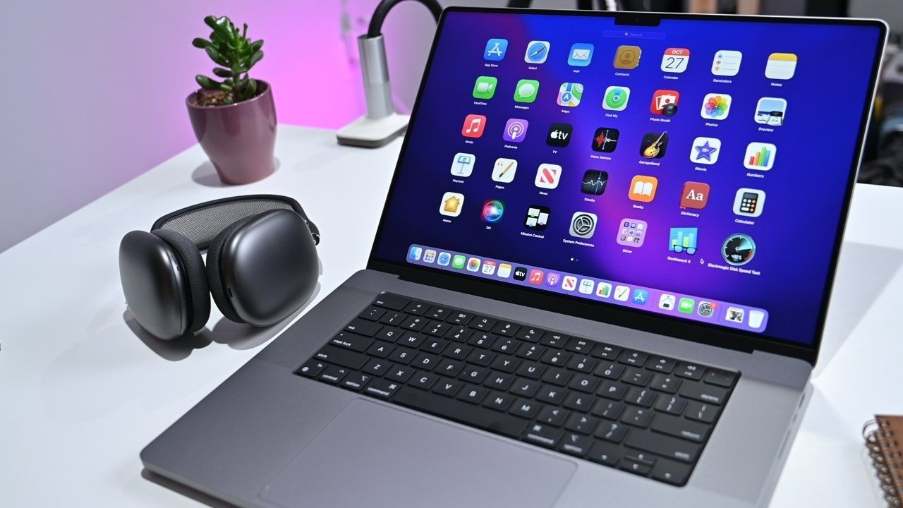 Laptop with colorful app icons on screen, headphones beside it, small potted plant in background, set on a white desk.
