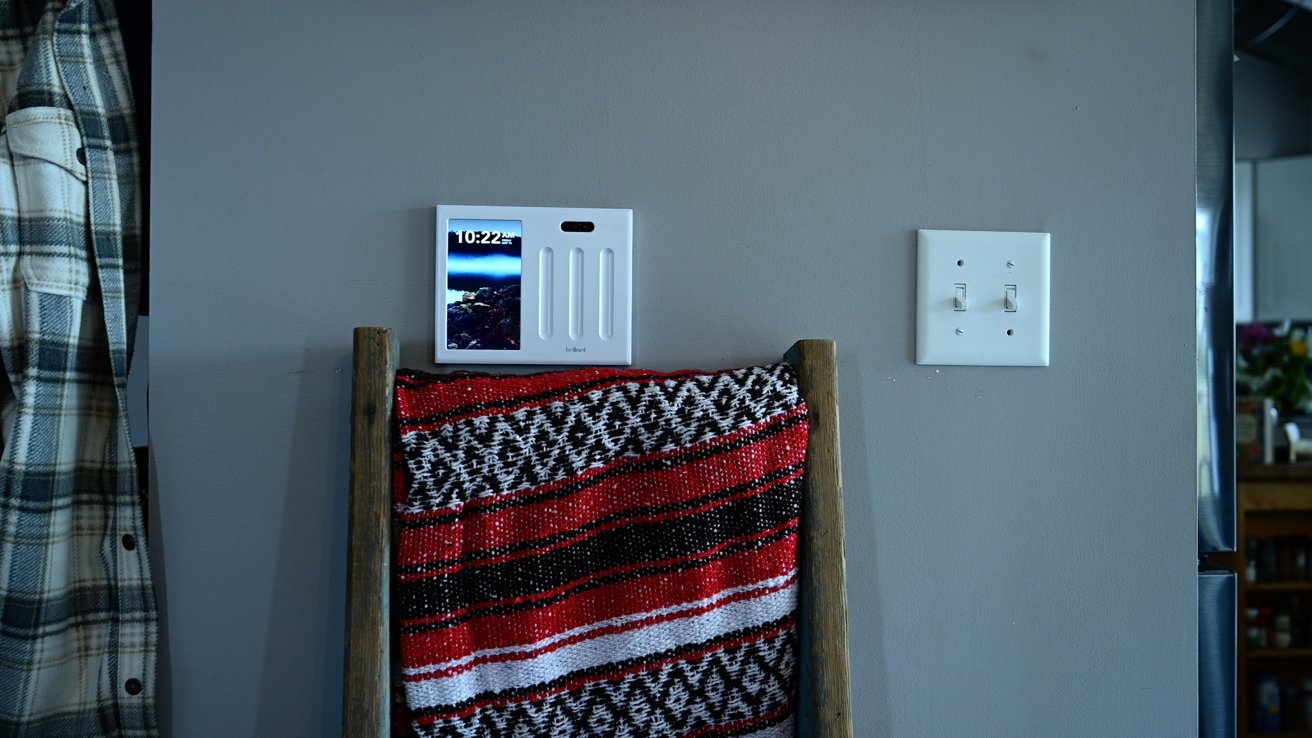 Smart light switch on a wall near a plaid shirt and a ladder with a red, black, and white patterned blanket.