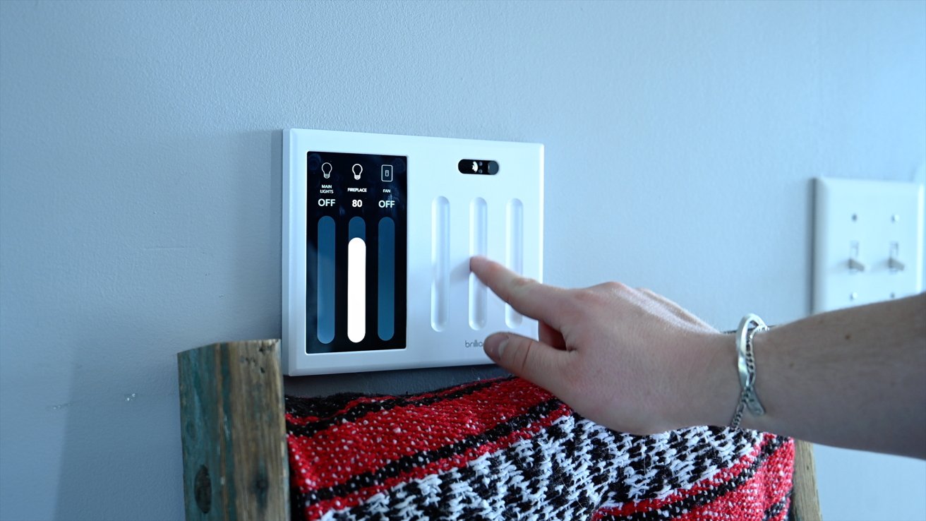 A hand interacts with a modern smart thermostat panel mounted on a wall, above a colorful patterned cloth.