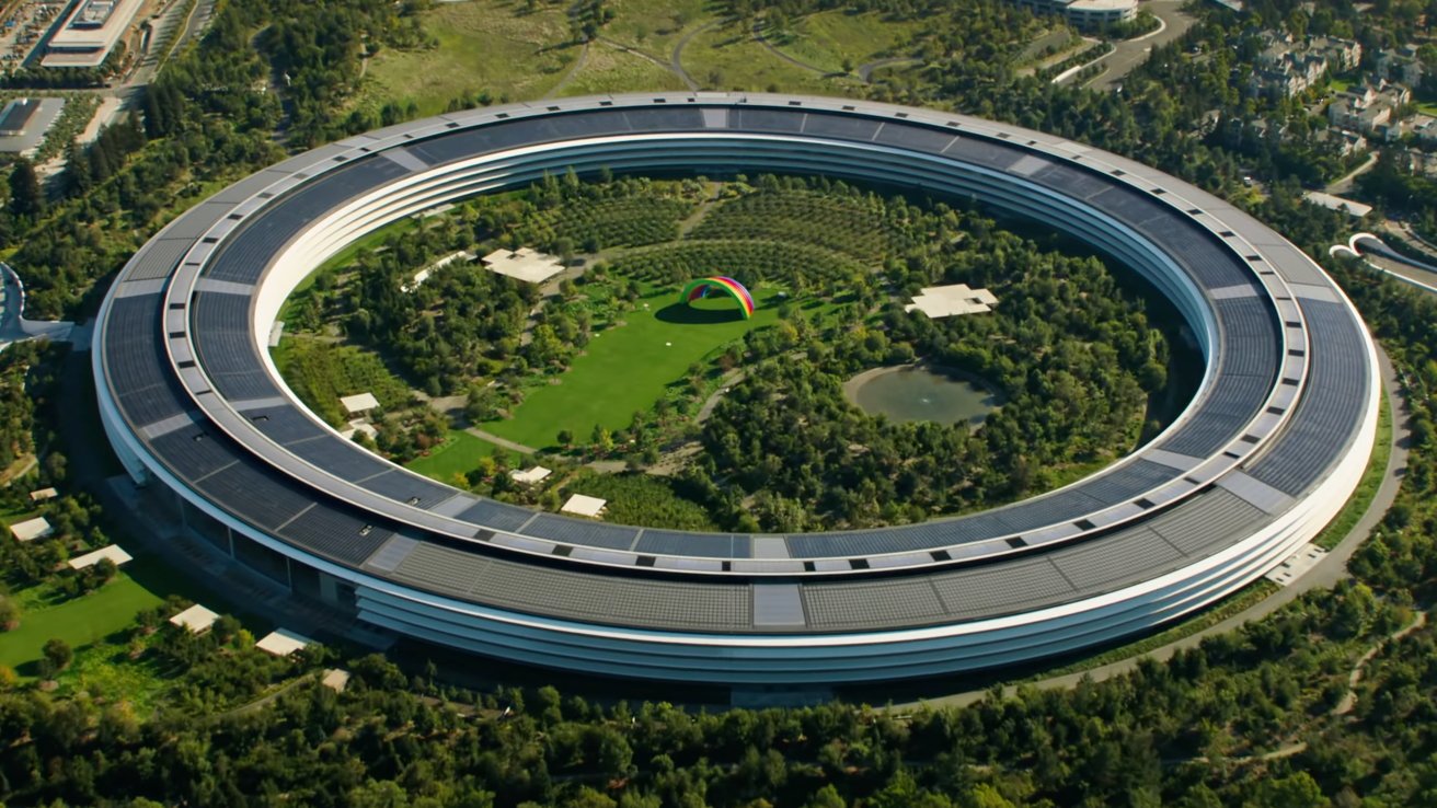 Aerial view of a circular building surrounded by greenery, with a vibrant rainbow structure and small pond inside the courtyard.