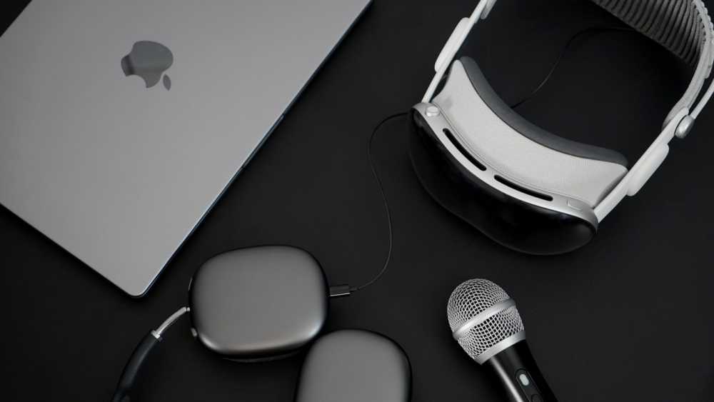 Laptop, futuristic 头显, wireless headphones, and a microphone arranged on a dark surface.