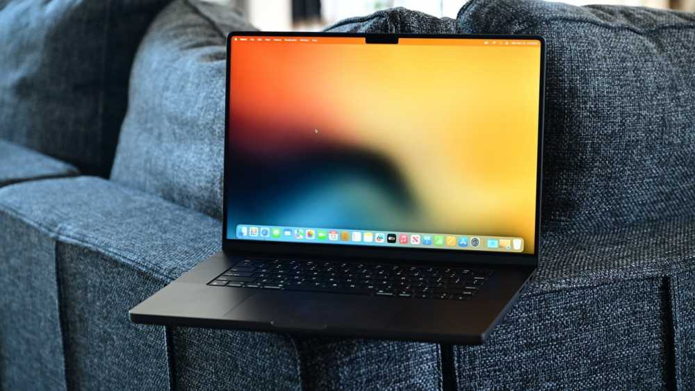 A laptop with a colorful screen sits on a gray fabric couch, displaying a blurred, vibrant abstract background.