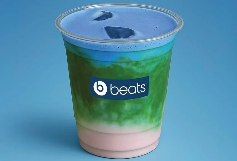 A colorful drink in a clear cup with blue, green, and pink layers, featuring a logo with the word 'beats' on a blue background.